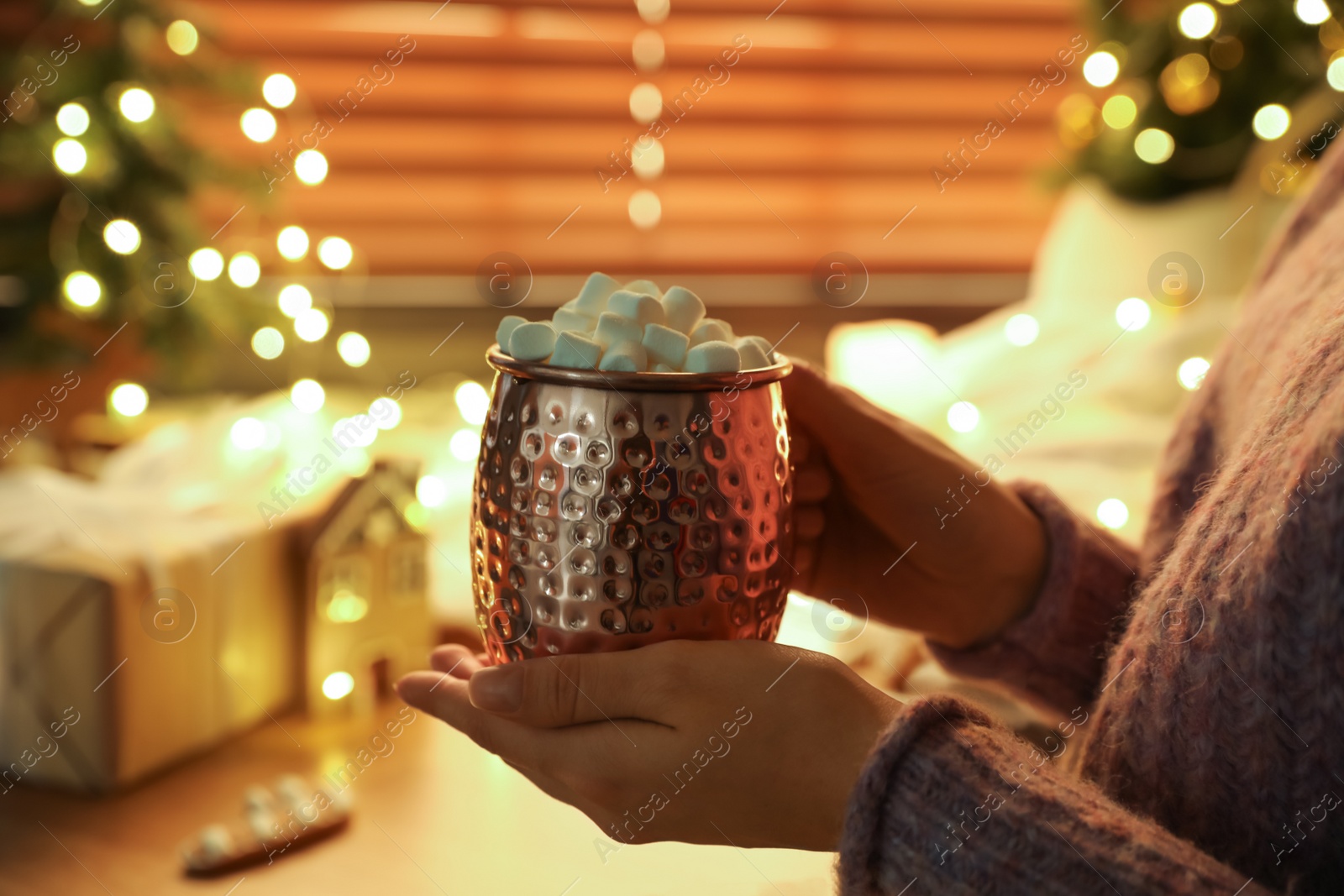 Photo of Woman holding cup of hot drink with marshmallows indoors, closeup. Magic Christmas atmosphere