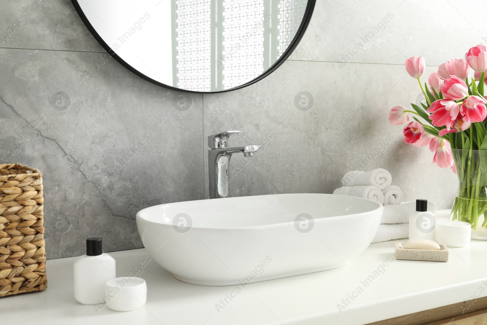 Photo of Vase with beautiful pink tulips and toiletries near sink in bathroom