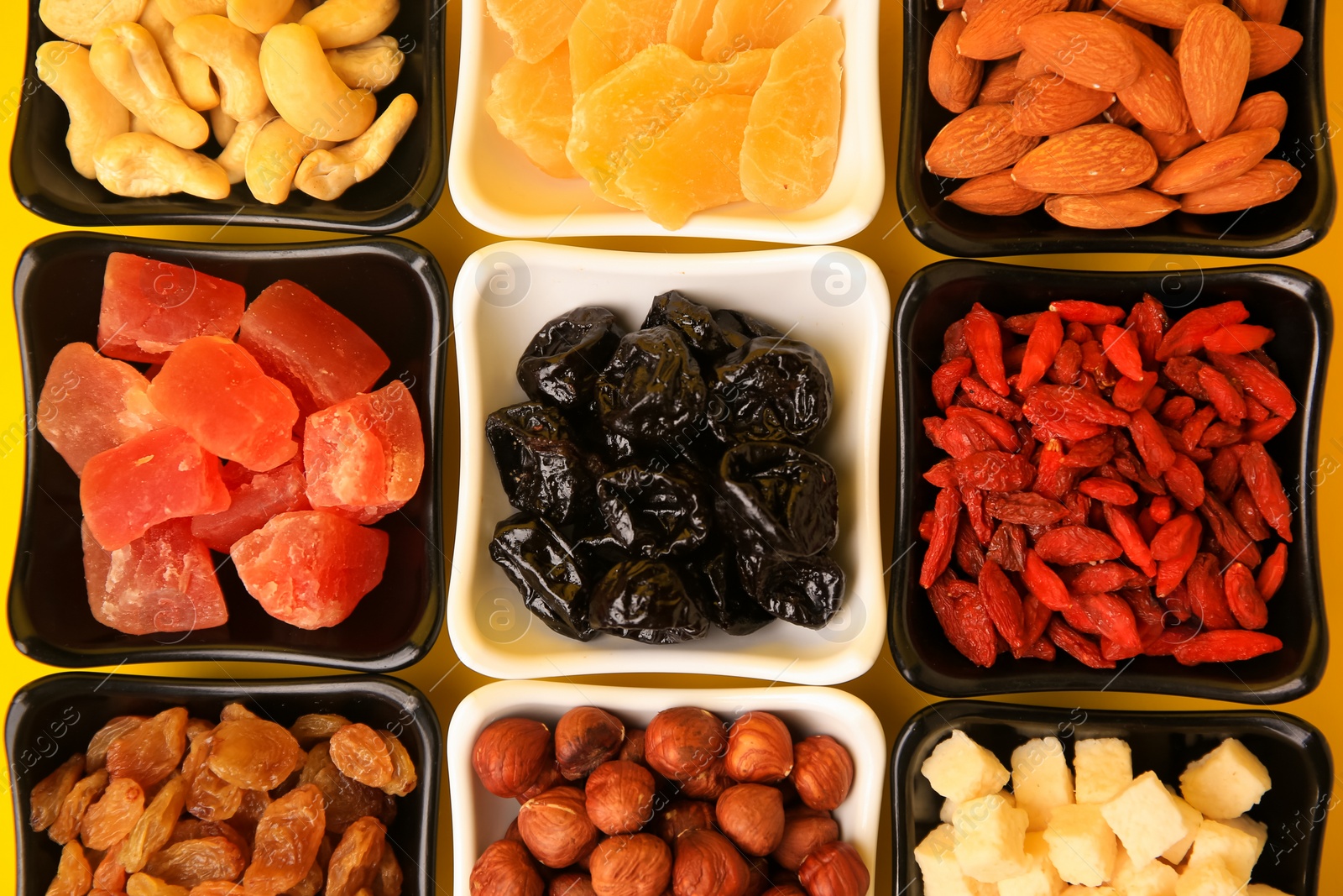 Photo of Bowls with dried fruits and nuts on yellow background, flat lay