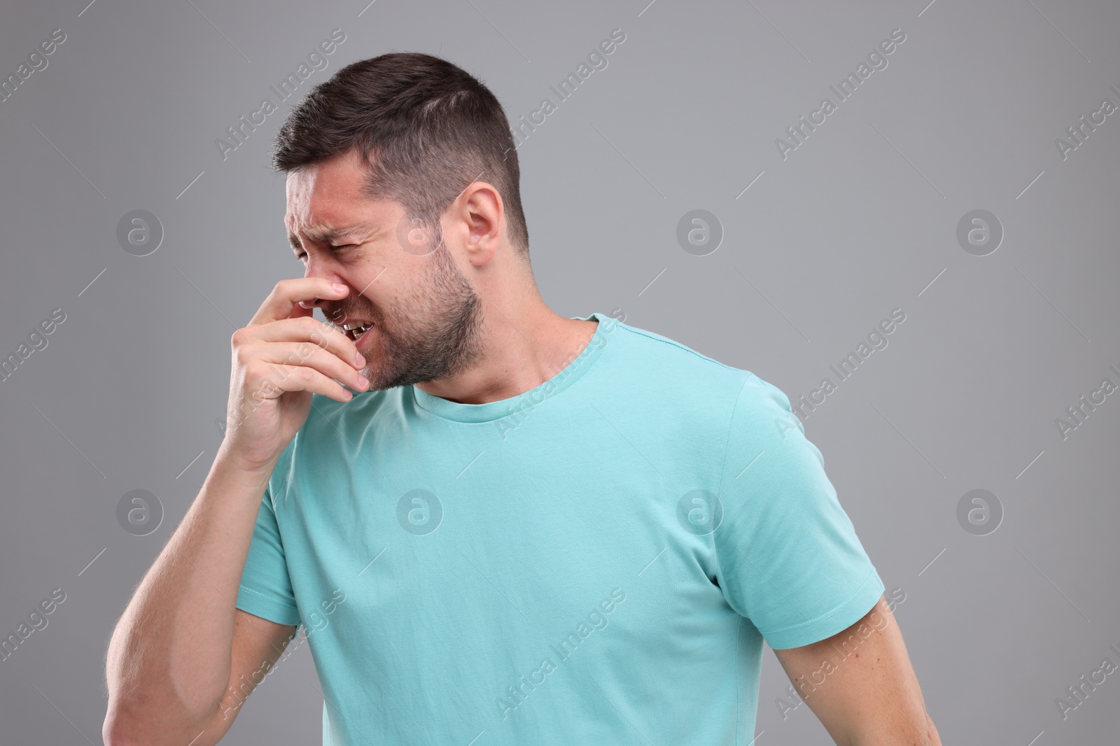 Photo of Allergy symptom. Man sneezing on light grey background