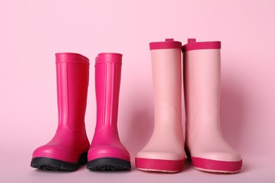 Two pairs of rubber boots on pink background