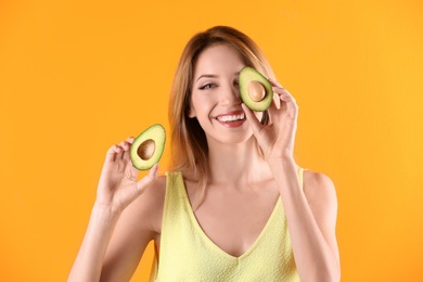 Portrait of young beautiful woman with ripe delicious avocado on color background