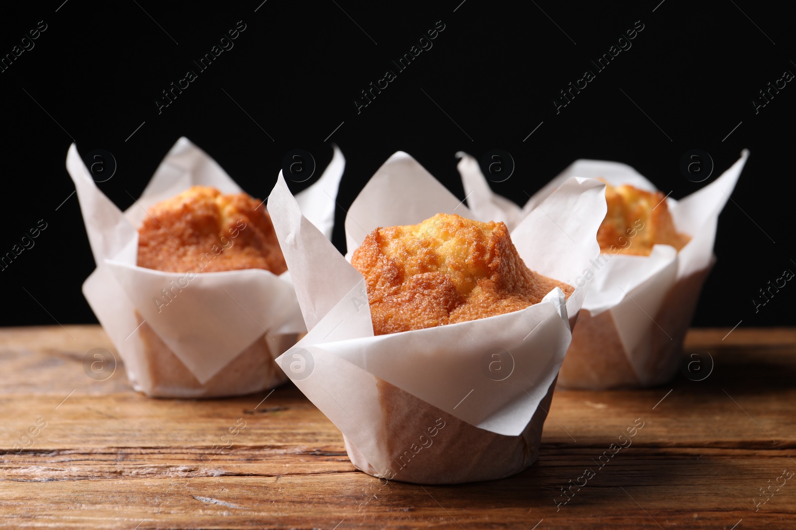 Photo of Delicious sweet muffins on wooden table against dark background, closeup