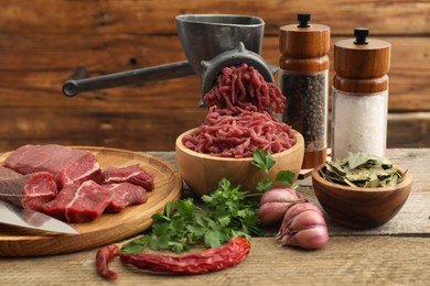 Photo of Manual meat grinder with beef, parsley and spices on wooden table