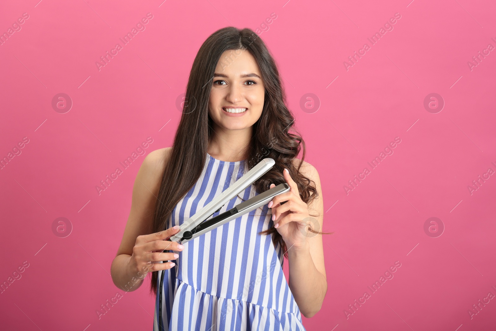 Photo of Young woman with modern hair iron on pink background, space for text