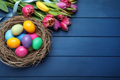 Photo of Bright painted eggs and spring tulips on blue wooden table, flat lay with space for text. Happy Easter