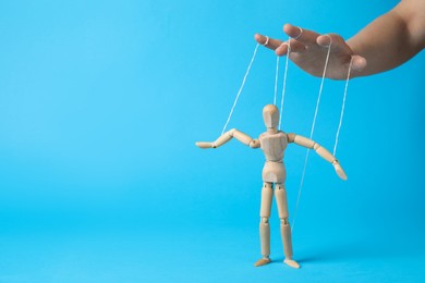 Photo of Woman pulling strings of puppet on light blue background, closeup. Space for text