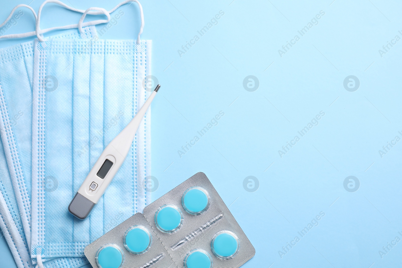 Photo of Thermometer, pills and respiratory masks on light blue background, flat lay. Space for text