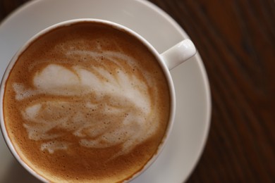 Cup of aromatic coffee with foam on wooden table, top view