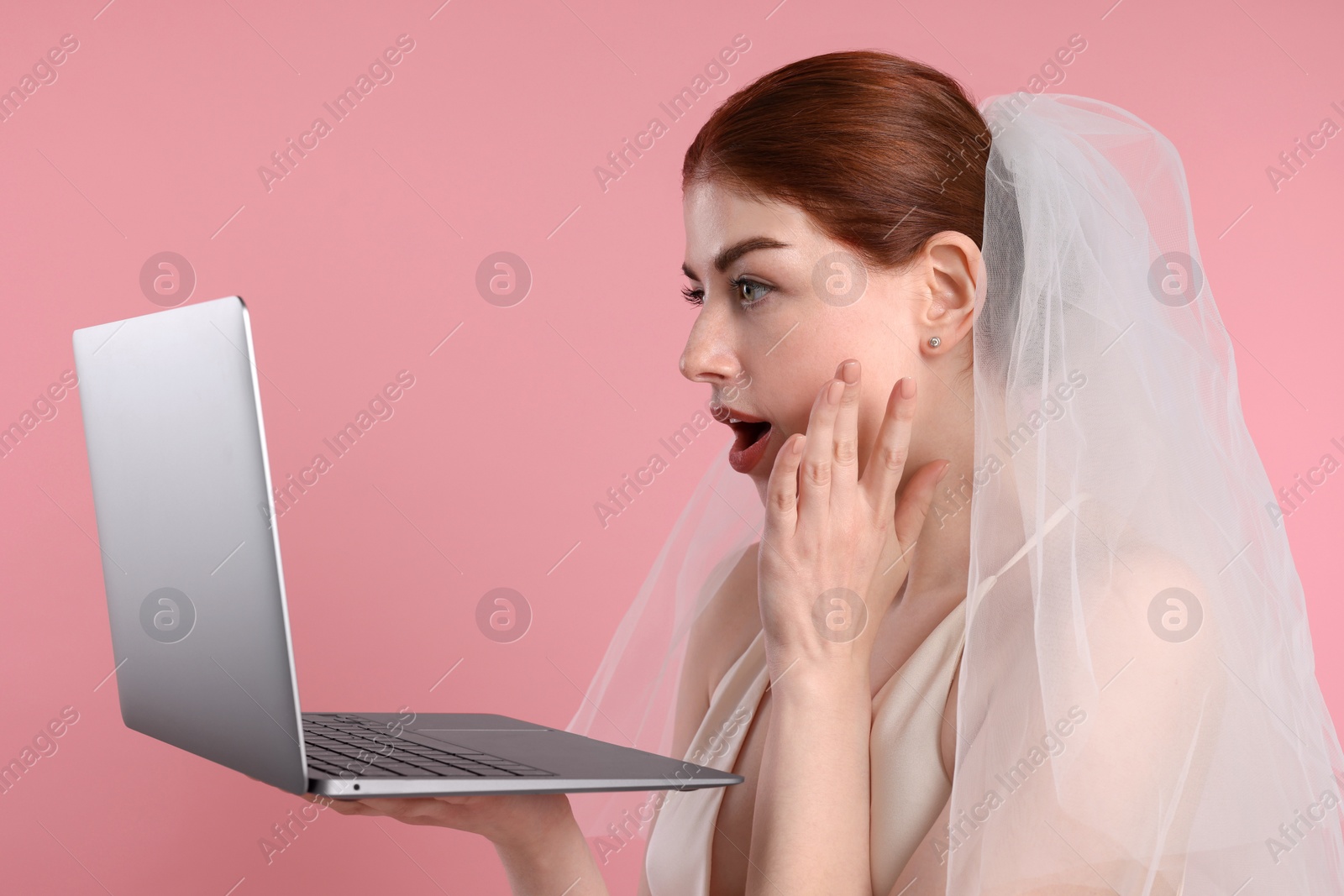 Photo of Surprised bride using laptop on pink background