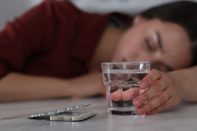 Woman with glass of water and antidepressant pills sleeping at white marble table, selective focus