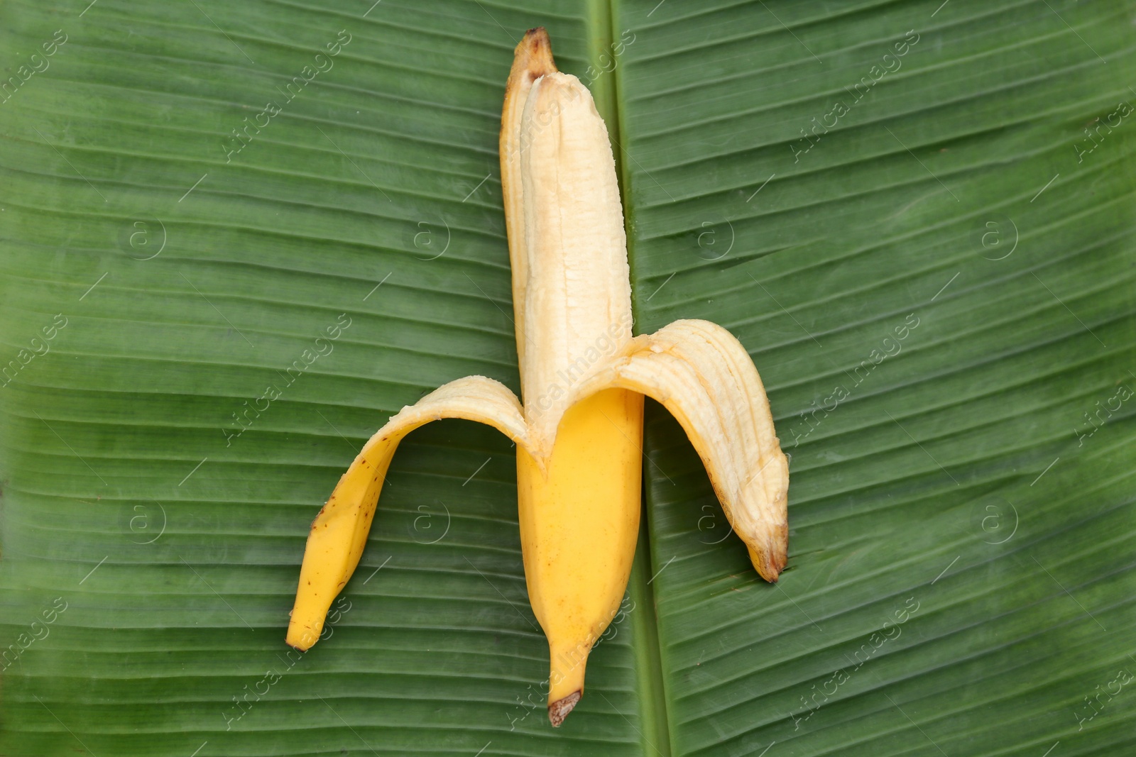 Photo of One delicious banana on fresh green leaf, top view