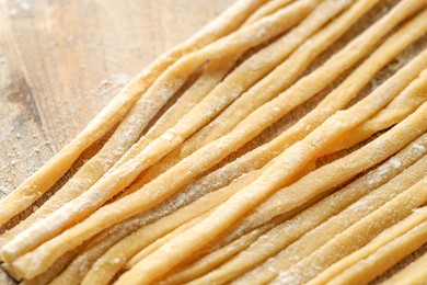 Photo of Raw homemade pasta and flour on wooden table, closeup