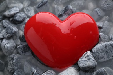 Red decorative heart on stones and water, closeup