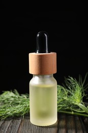 Photo of Bottle of essential oil and fresh dill on dark wooden table against black background, closeup