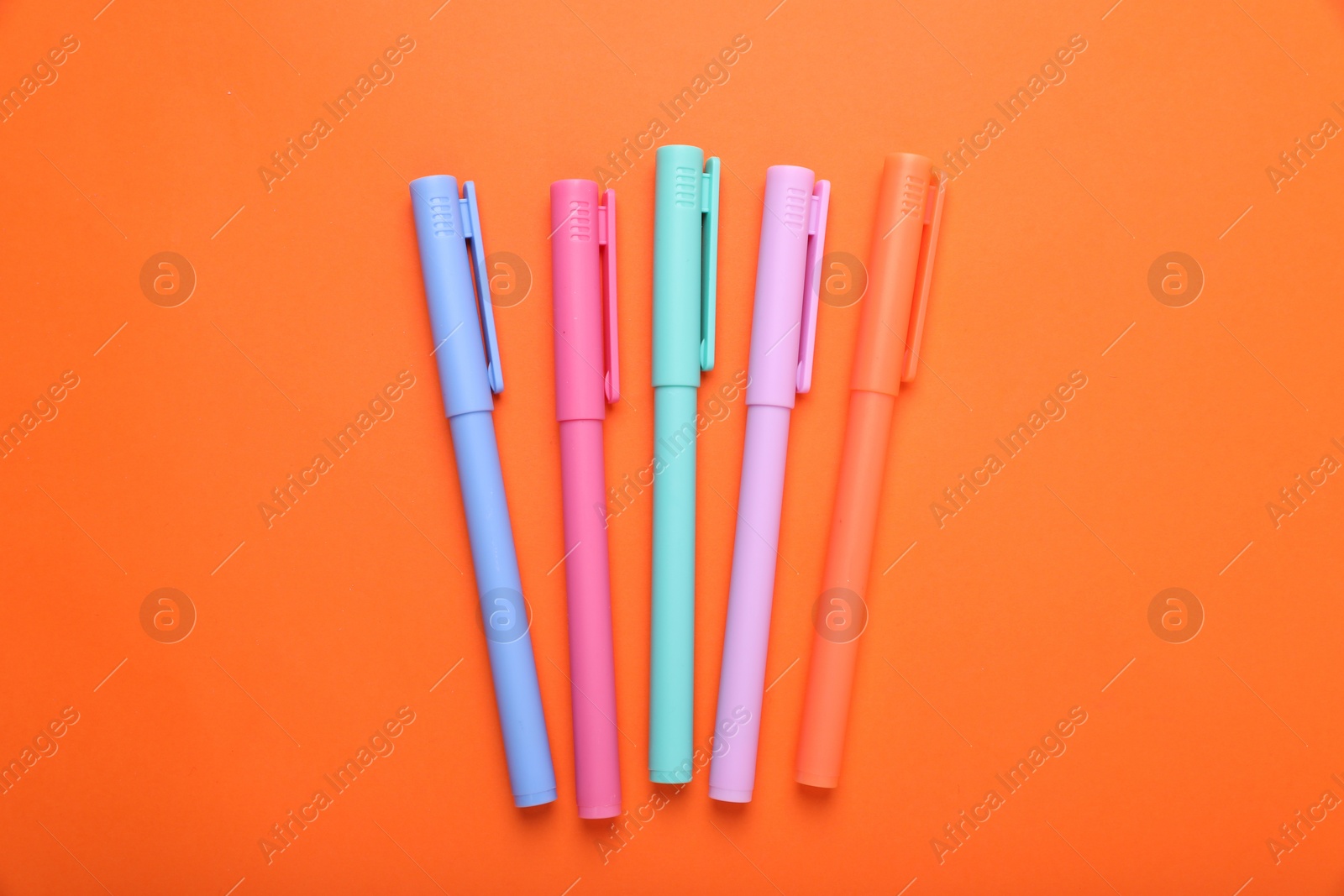 Photo of Many colorful markers on orange background, flat lay