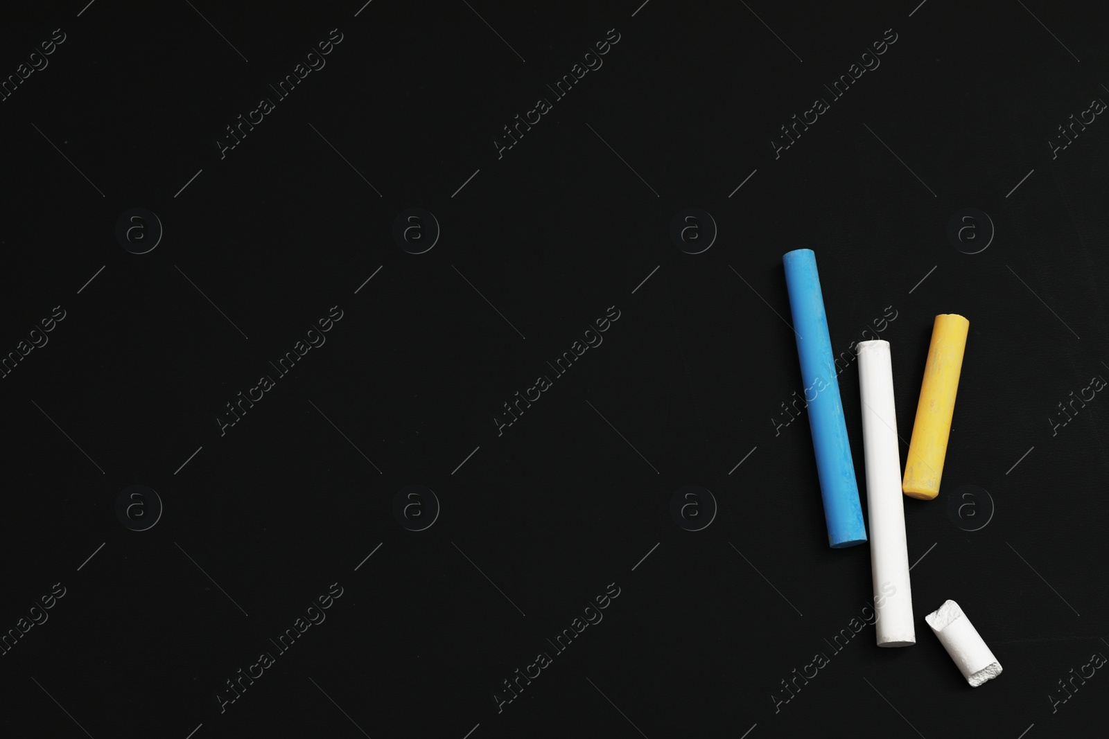 Photo of Colorful chalks on black board, flat lay. Space for text