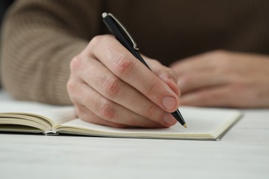 Photo of Man writing in notebook at white table, closeup