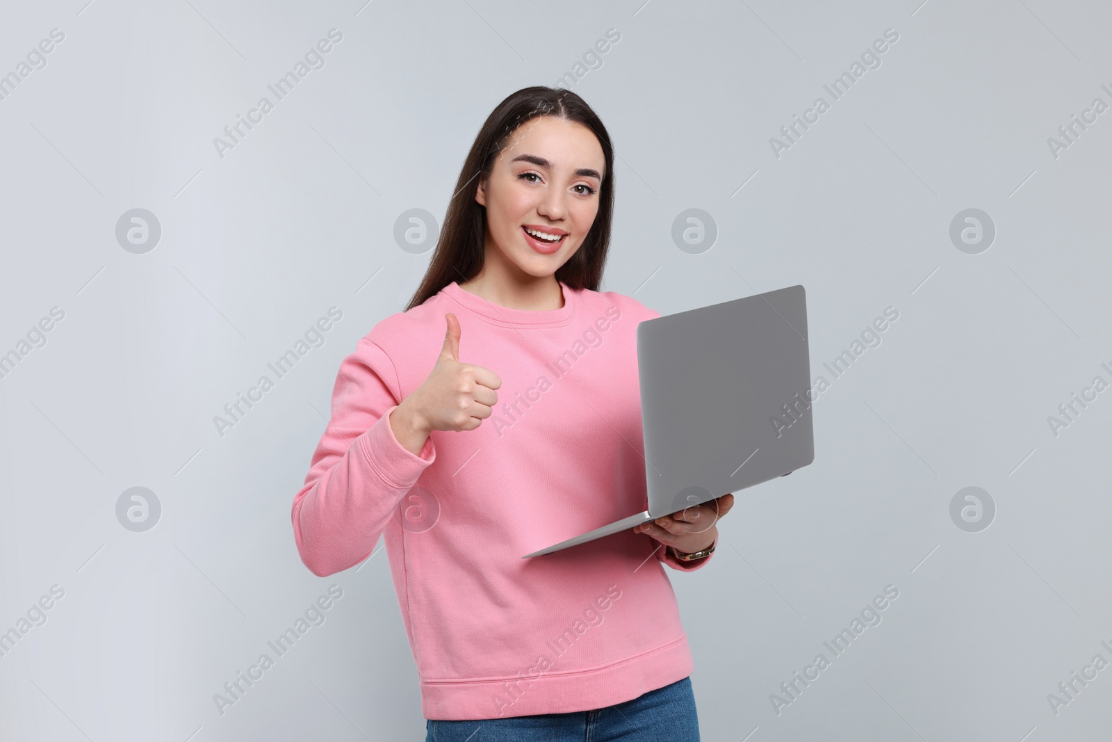 Photo of Smiling young woman with laptop showing thumbs up on grey background, space for text