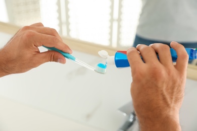 Man applying toothpaste on brush in bathroom, closeup