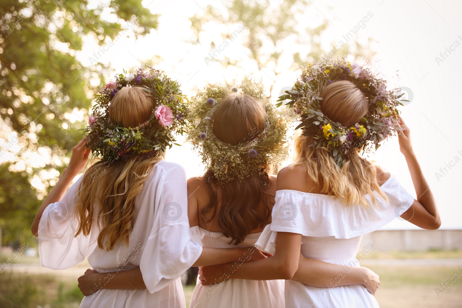 Photo of Young women wearing wreaths made of beautiful flowers outdoors on sunny day, back view