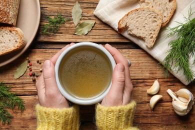 Photo of Woman with cup of hot delicious bouillon at wooden table, top view