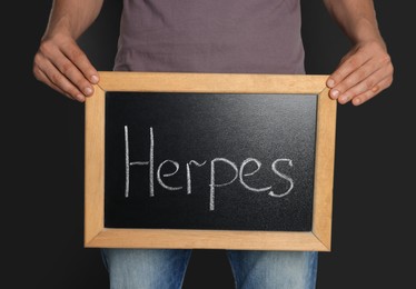 Photo of Man holding small chalkboard with word Herpes on black background