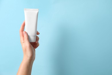 Photo of Woman with tube of hand cream on light blue background, closeup. Space for text