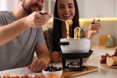 Affectionate couple enjoying cheese fondue during romantic date in kitchen, closeup