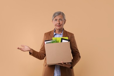 Photo of Confused unemployed senior woman with box of personal office belongings on beige background
