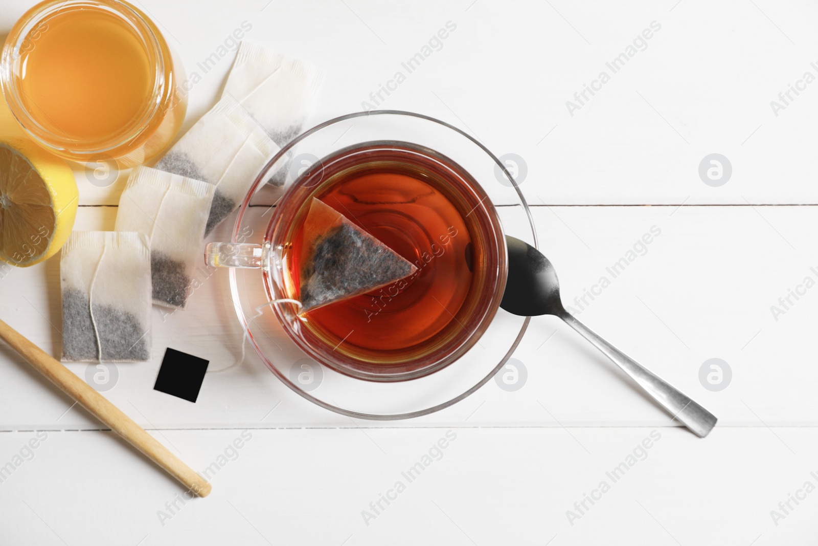 Photo of Tea bags, honey and lemon near cup of hot drink on white wooden table, flat lay