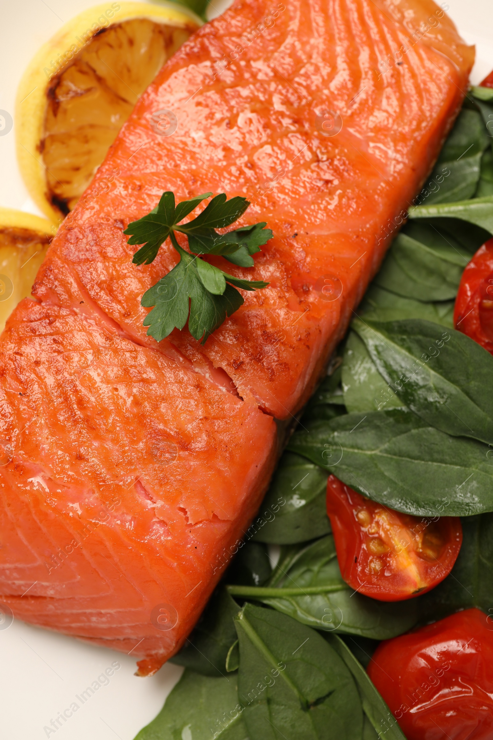 Photo of Tasty grilled salmon with basil, tomatoes and lemon on white plate, top view