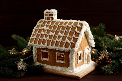 Photo of Beautiful gingerbread house decorated with icing and fir branch on wooden table