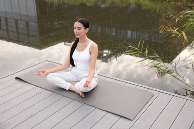 Beautiful young woman practicing Padmasana on yoga mat outdoors, above view. Lotus pose