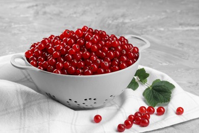 Photo of Ripe red currants in colander and leaves on grey textured table
