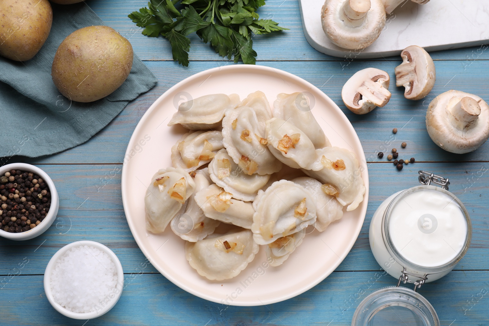 Photo of Delicious dumplings (varenyky) with potatoes and onion served on light blue wooden table, flat lay