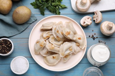 Delicious dumplings (varenyky) with potatoes and onion served on light blue wooden table, flat lay