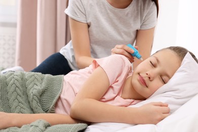 Mother dripping medication into daughter's ear in bedroom