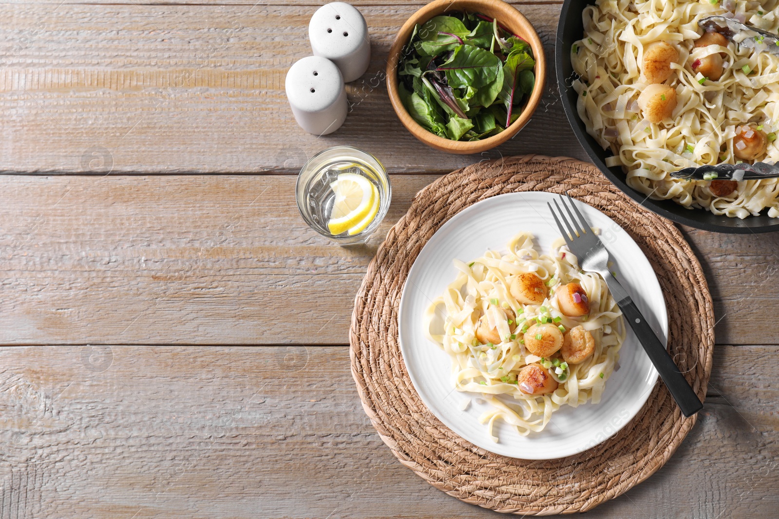 Photo of Delicious scallop pasta with onion served on wooden table, flat lay. Space for text