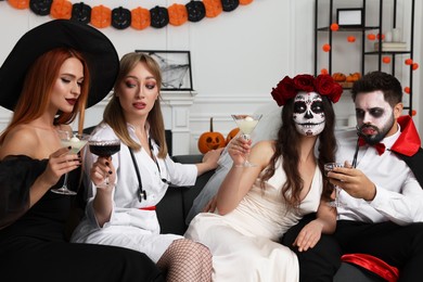 Group of people in scary costumes with cocktails celebrating Halloween indoors