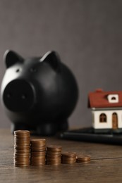 Photo of House model, piggy bank, calculator and stacked coins on wooden table, selective focus