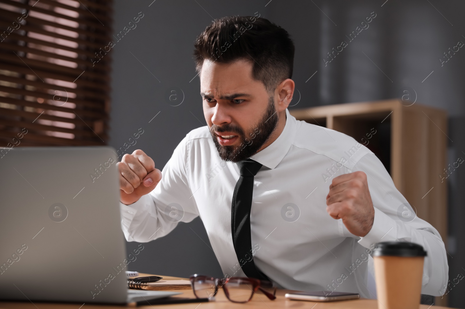 Photo of Emotional young businessman working on laptop in office. Online hate concept