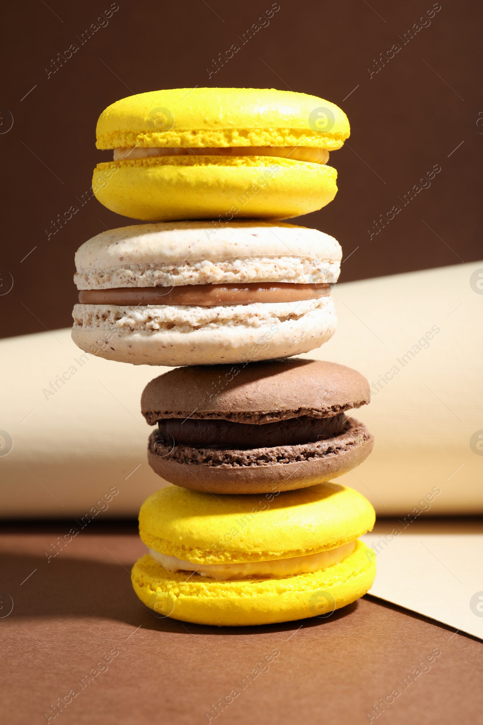 Photo of Stack of colorful macarons and paper roll on brown background