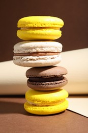 Photo of Stack of colorful macarons and paper roll on brown background