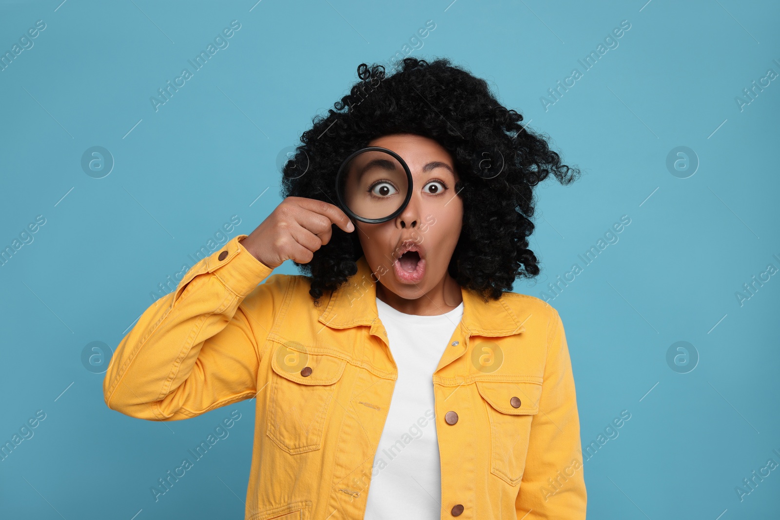 Photo of Emotional woman looking through magnifier glass on light blue background