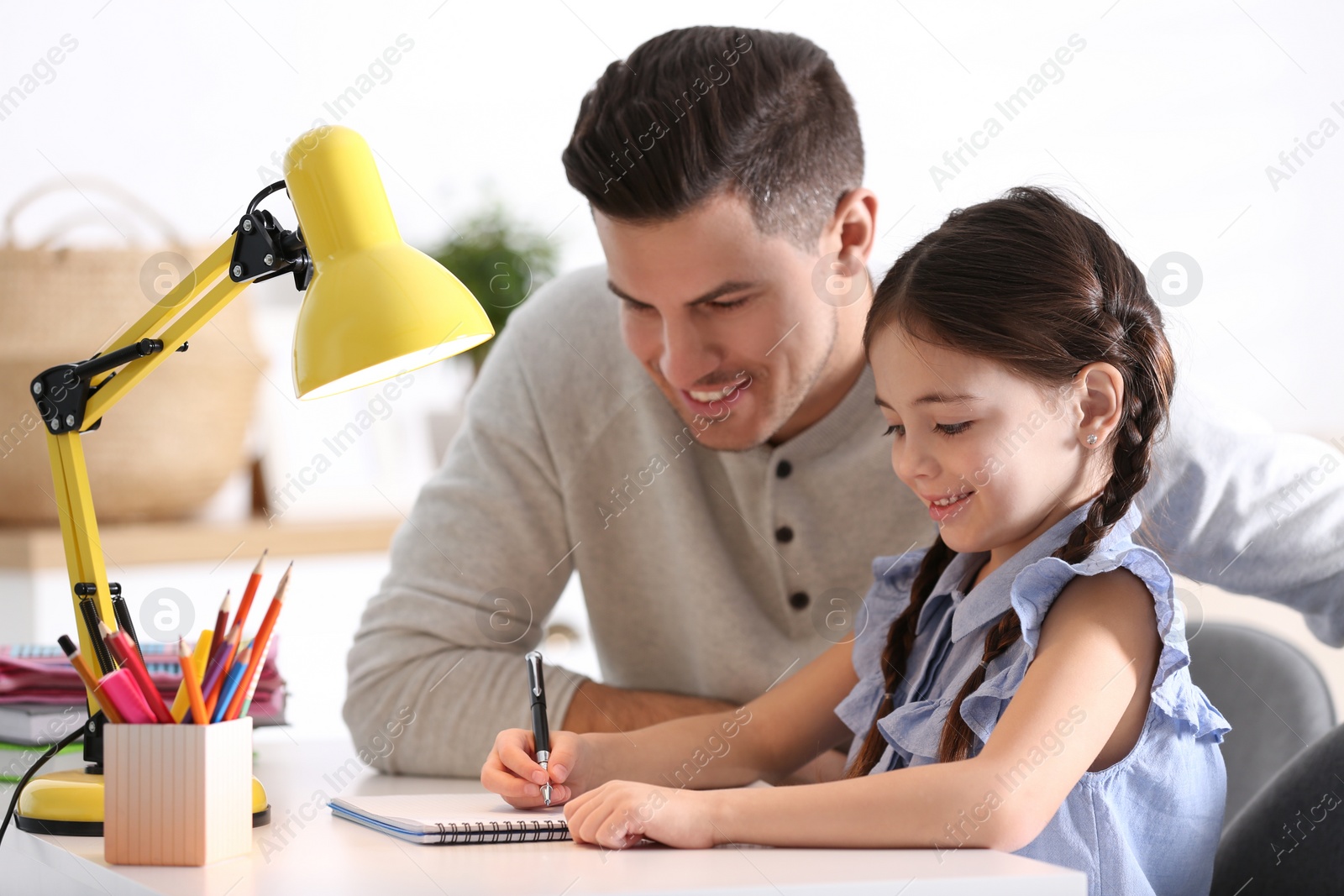 Photo of Man helping his daughter with homework at table indoors