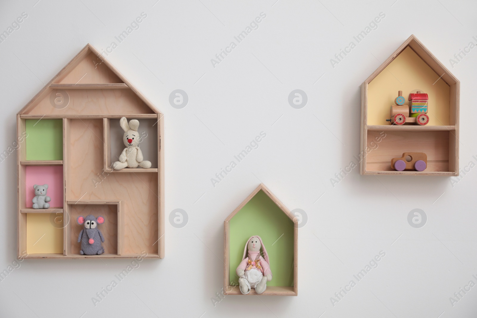 Photo of Stylish house shaped shelves with toys on white wall. Baby room interior design