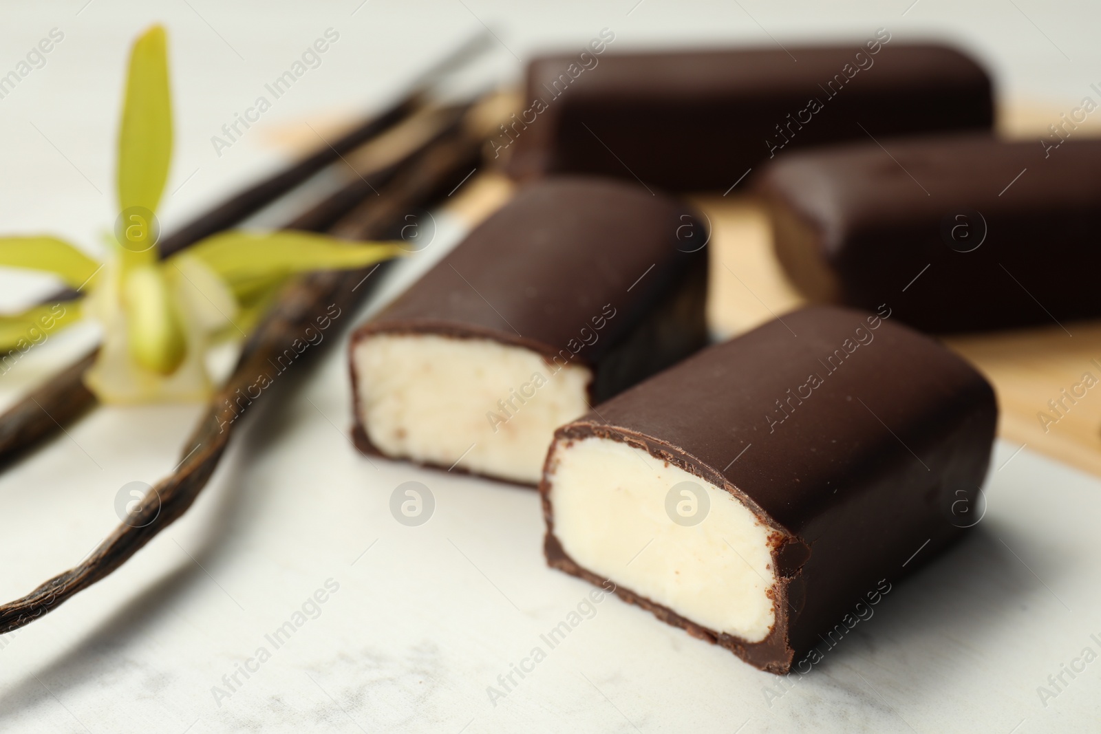 Photo of Glazed curd cheese bars, vanilla pods and flower on white table, closeup