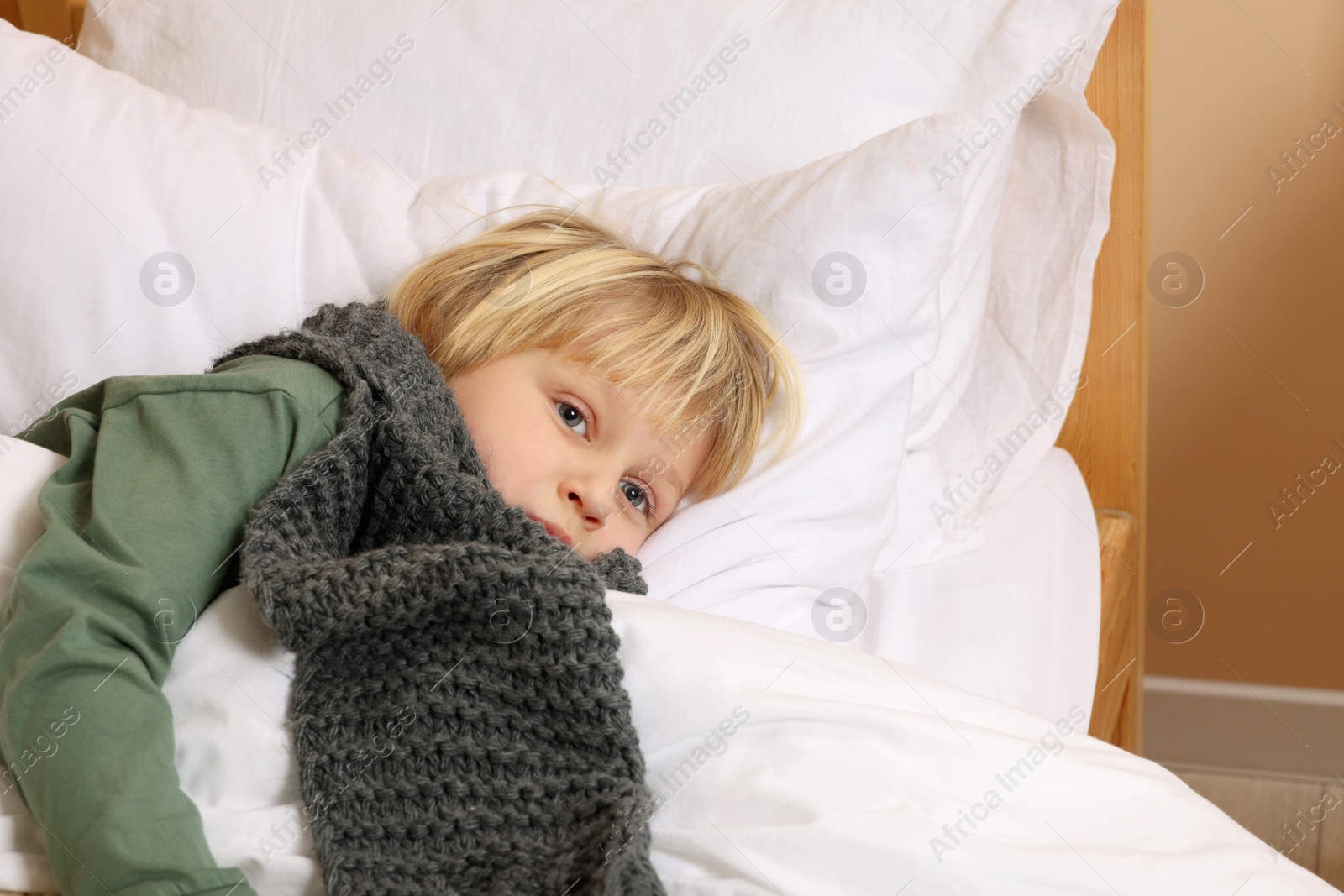 Photo of Sick boy with scarf around neck lying in bed indoors