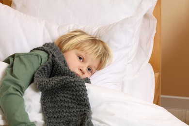 Photo of Sick boy with scarf around neck lying in bed indoors